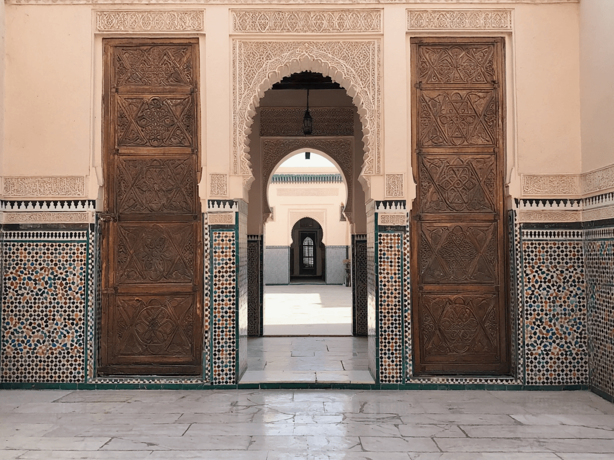 Visuel d’inspiration — Portes de bois sculpte et zellige encadrant une cour interieure marocaine.