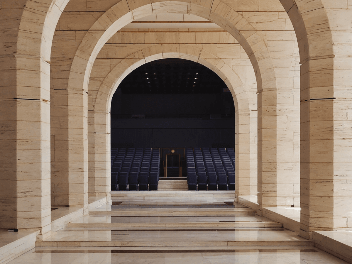 Visuel d’inspiration — Arcades de pierre claire ouvrant sur un auditorium aux fauteuils bleus, pret a accueillir une seance.